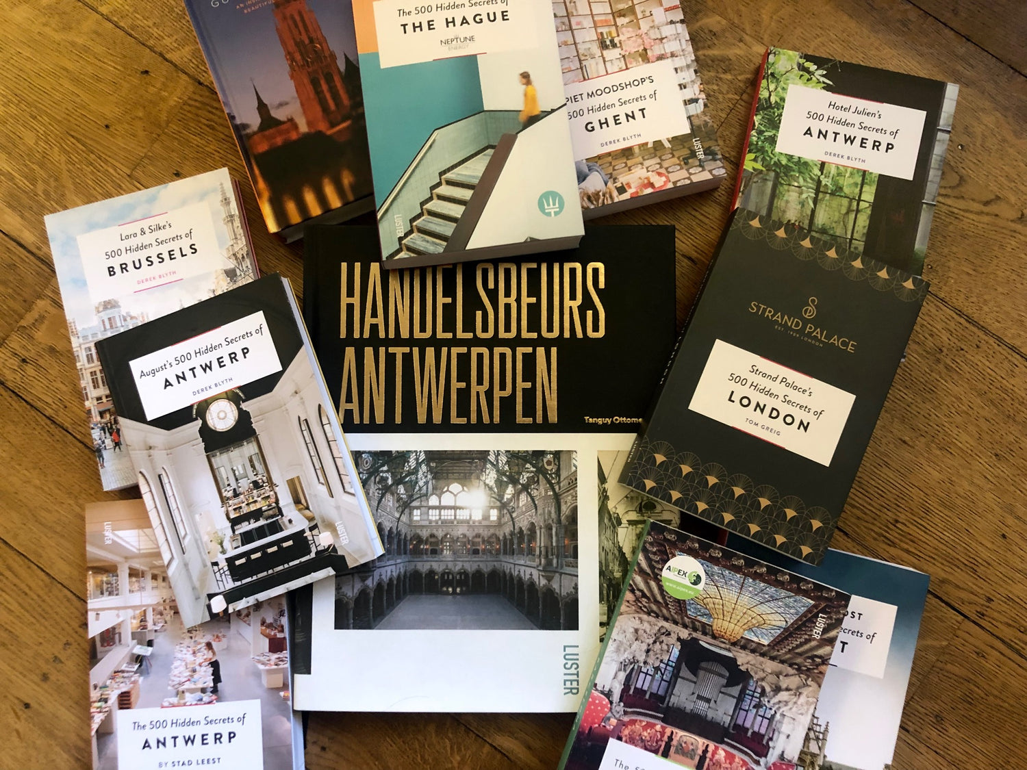 Personalised books by Luster Publishing spread out across the floor and photographed from above. A book on the Antwerp Stock Exchange in the middle surrounded by several customised guides from The 500 Hidden Secrets series