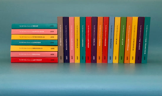 Colourful backs of The 500 Hidden Secrets series of travel guides, stacked on a light blue bench